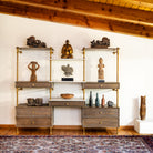 A set of storage drawers and shelves with aged brass legs, cement gray wood, and various decorative items on the shelves.