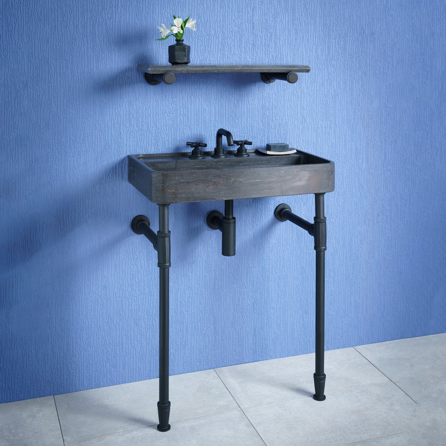 A small rectangular honed antique gray limestone Lumbre bath sink on matte black elemental facet vanity legs. with an accessory shelf.