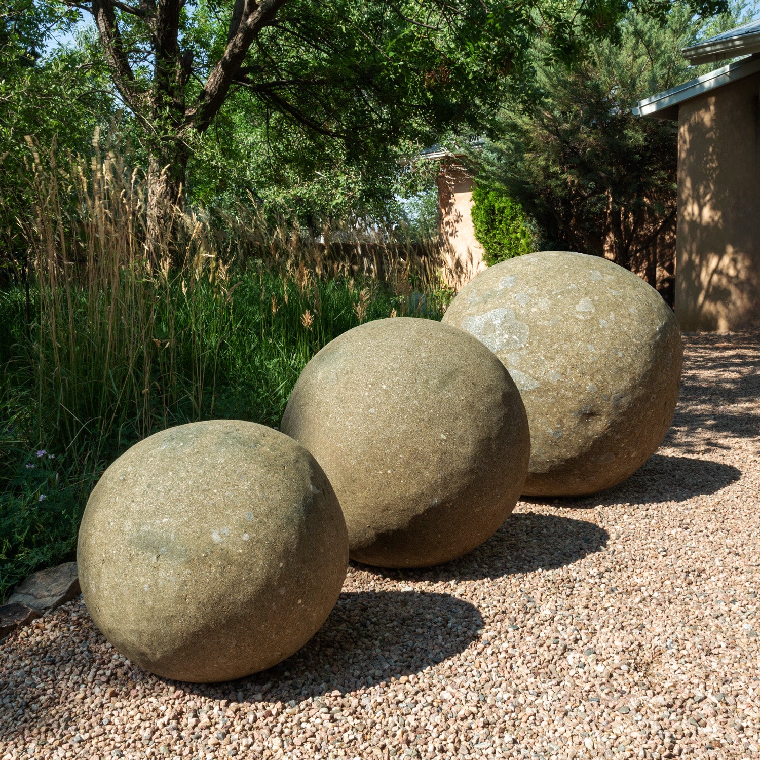 Three large stone spheres on a gravel surface with greenery in the background