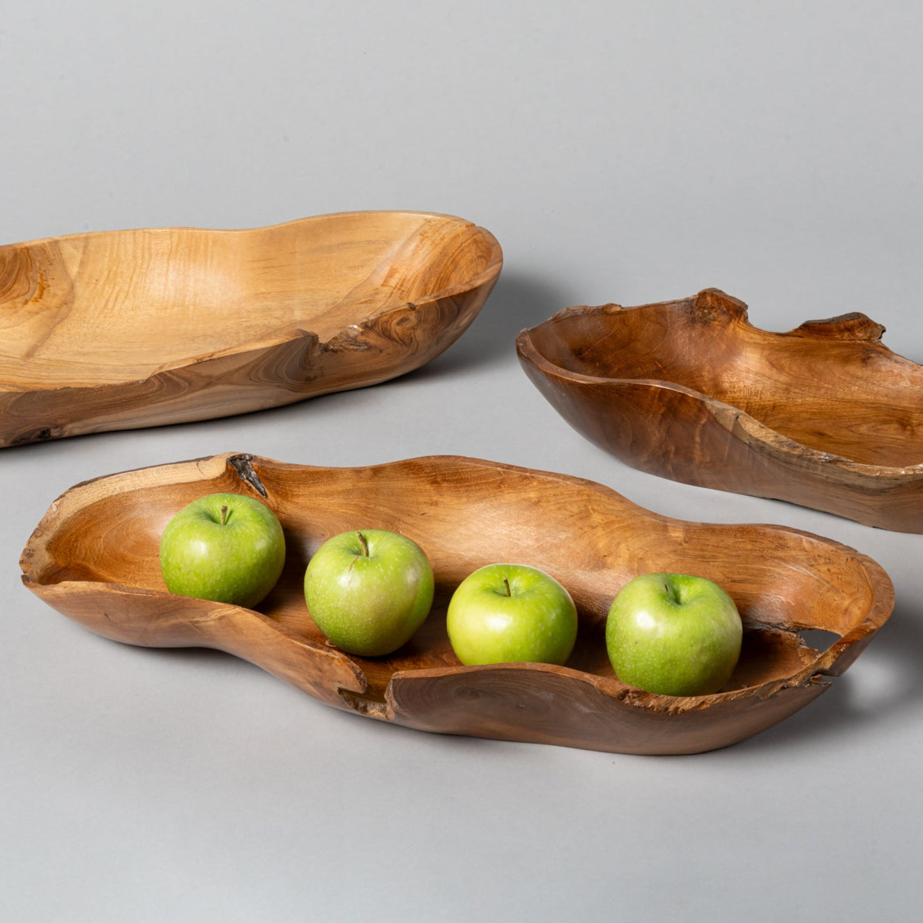 A set of three hand-carved wooden bowls of varying sizes, with the largest bowl containing three green apples.