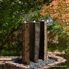 A vertical, columnar basalt fountain installed on a bed of pebbles, with natural weathered exterior and mirror polish surfaces.