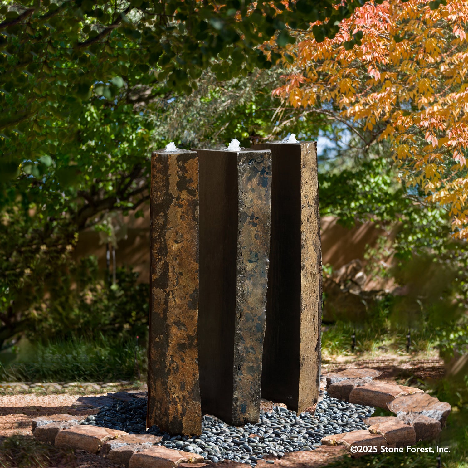 A vertical, columnar basalt fountain installed on a bed of pebbles, with natural weathered exterior and mirror polish surfaces.