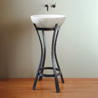 Carrara Marble sink on an Iron Pedestal against a plain wall.
