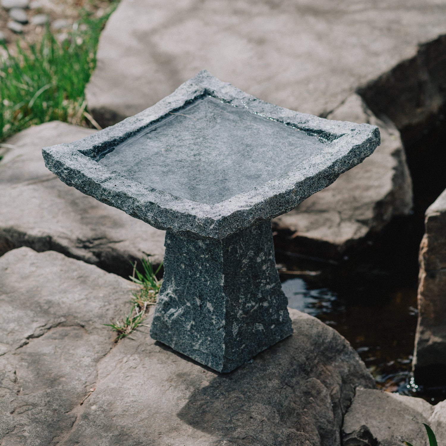 This birdbath is hand-carved from blue-gray granite with a rough chiseled finish
