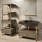 A Terra Bath Sink with aged brass legs, placed on a console stand, accompanied by a drawer vanity with a cement gray wood drawer. The backdrop features a tiled wall and a mirror.