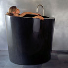 The Stone Forest Oval Soaking Tub is carved in a monumental block of black granite with a polished finish. This Bathtub is made on a custom basis only.